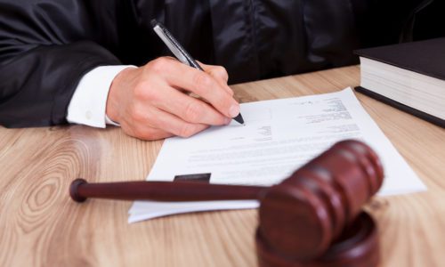 Male judge signing papers with a gavel in front of him