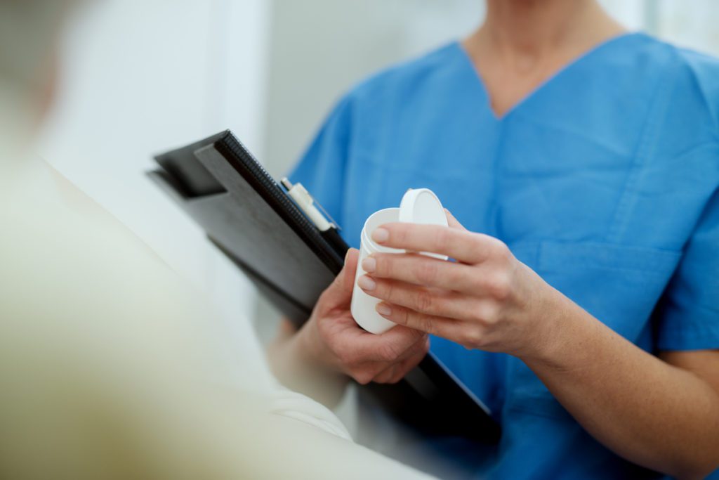 Close up view of nurses hands holding patient medications and papers.