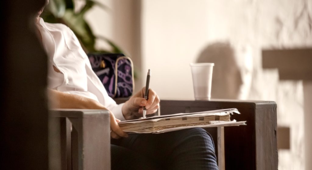 California Physchology License photo of person sitting in two toned room holding pen and pad with only torso and legs showing